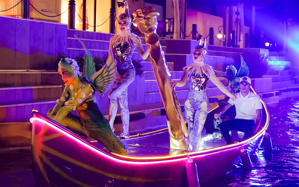 Performers in costumes on a lit boat during the Land of Legends Night Show parade.