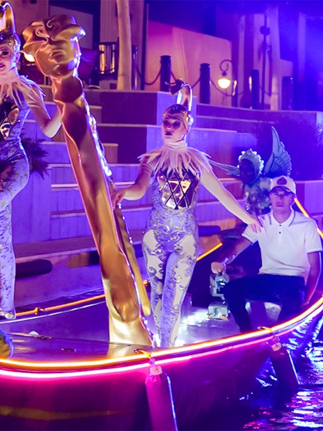 Performers in costumes on a lit boat during the Land of Legends Night Show parade.