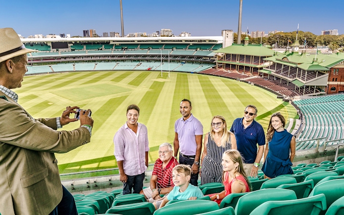 Tour group at Sydney Cricket Ground with guide taking a photo in the stadium seats.