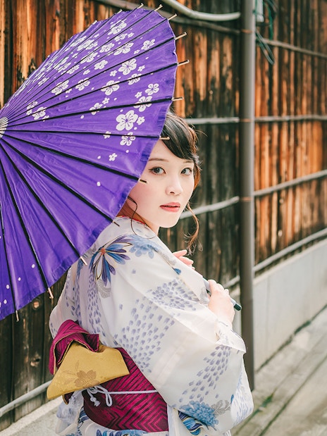 Girl in kimono holding violet umbrella on traditional Japanese street.