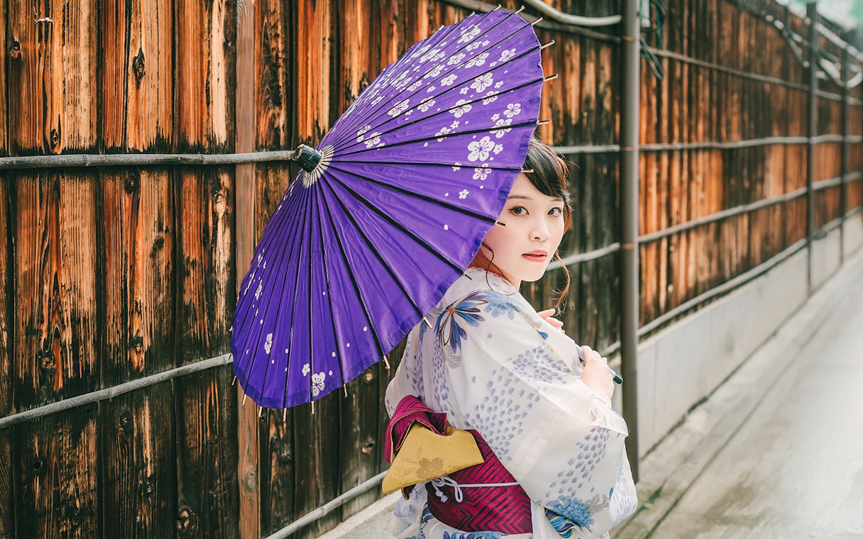 Girl in kimono holding violet umbrella on traditional Japanese street.