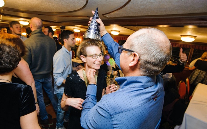 Guests celebrating on a New Year’s Eve cruise in Budapest with party hats and live music.