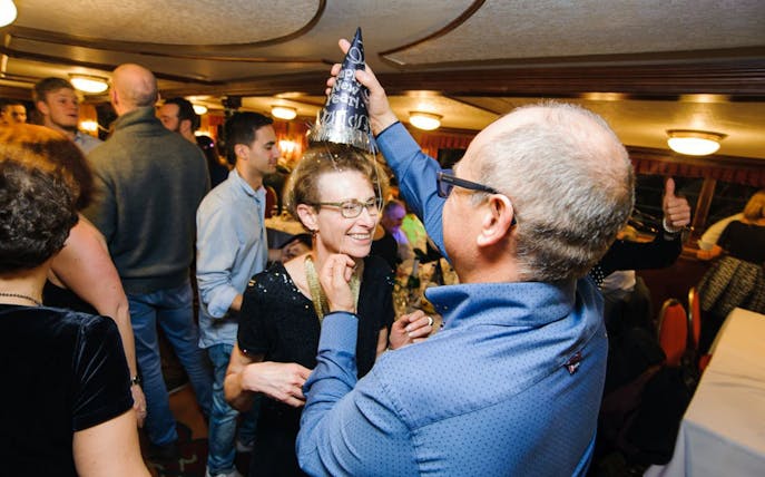Guests celebrating on a New Year’s Eve cruise in Budapest with party hats and live music.