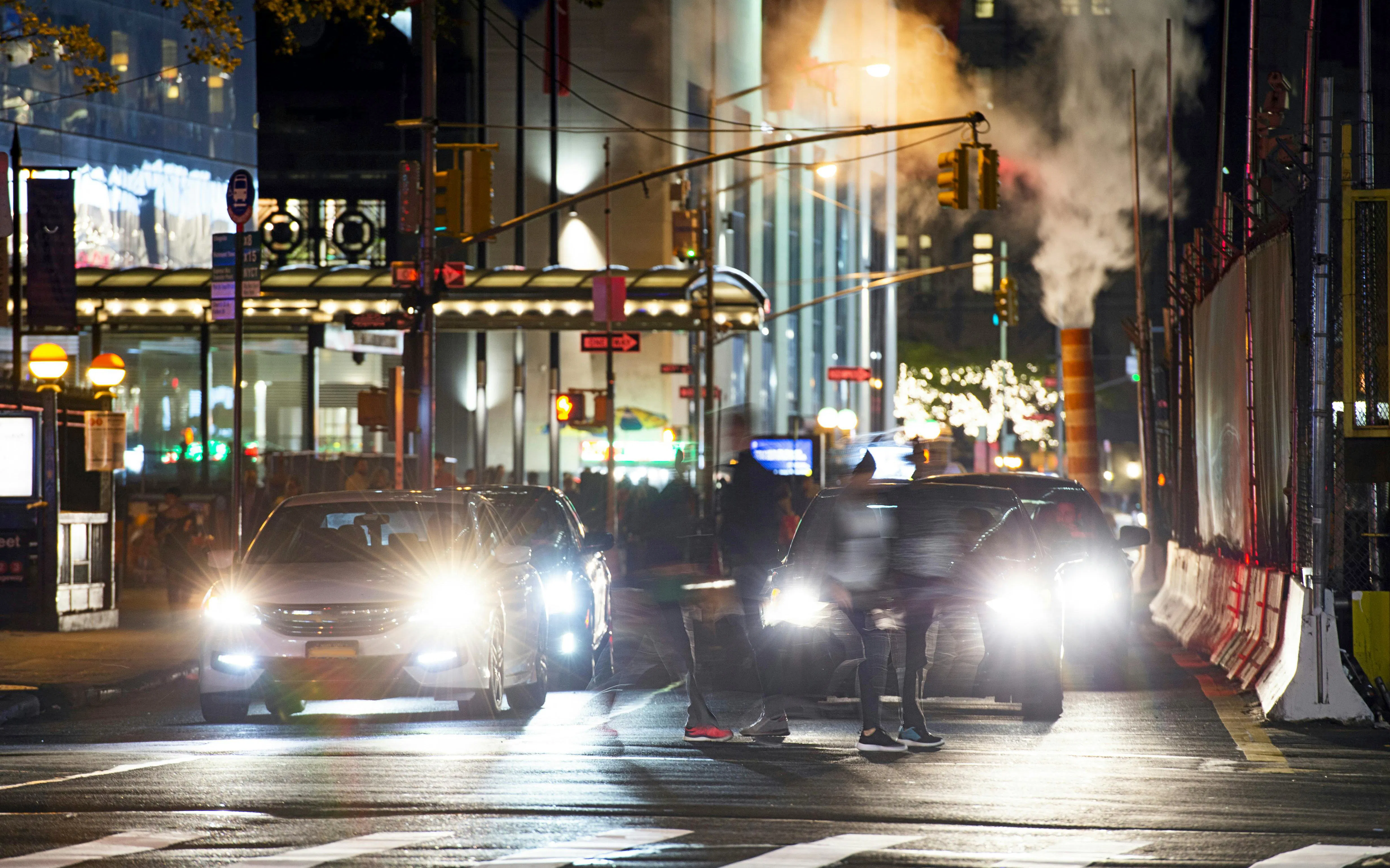 Busy Manhattan street intersection at night with cars and blurred pedestrians, New York City.