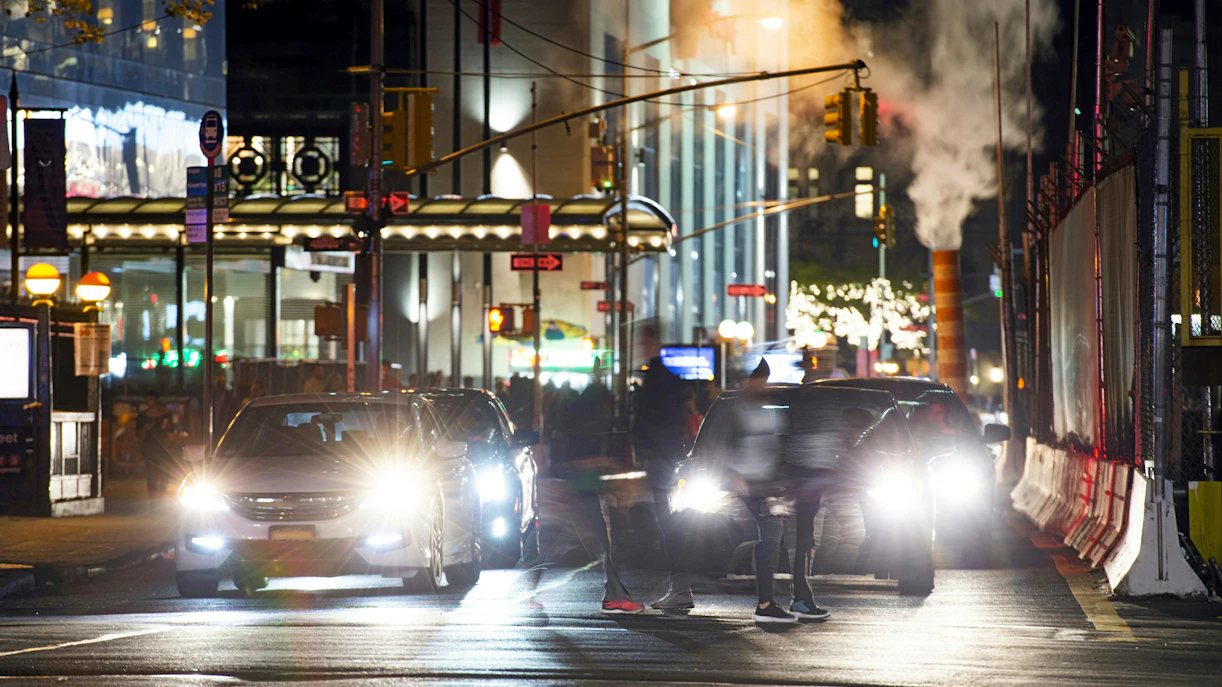 Busy Manhattan street intersection at night with cars and blurred pedestrians, New York City.