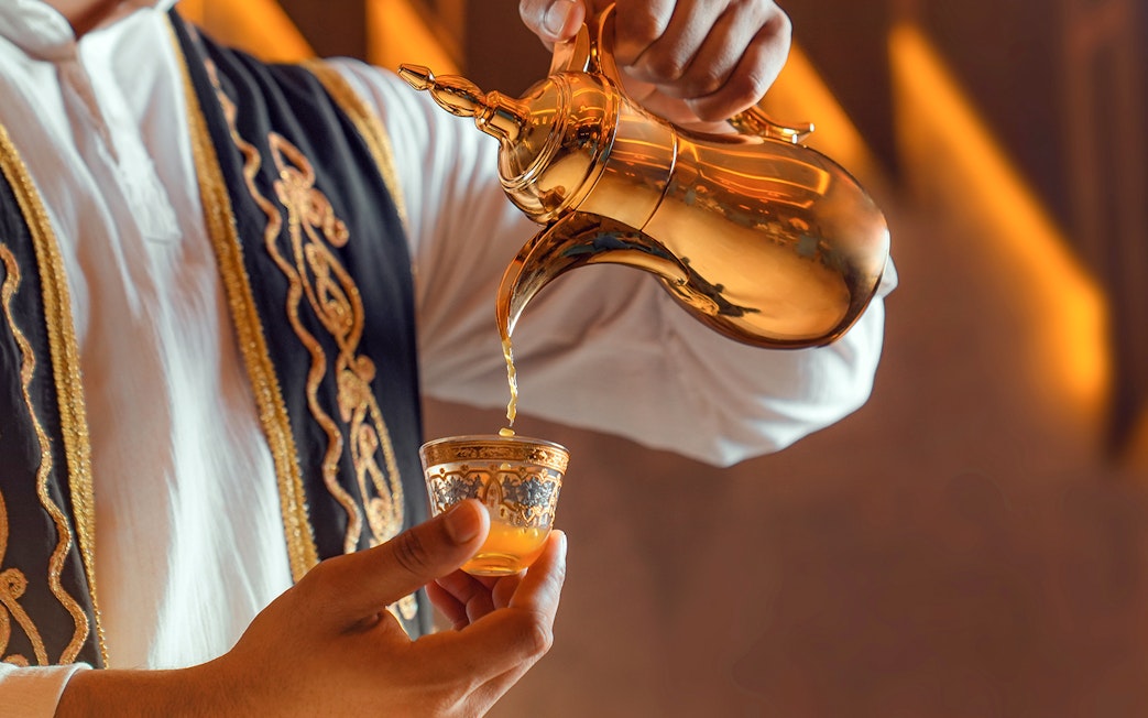 Traditional Arabic coffee being poured from a golden pot into an ornate cup.