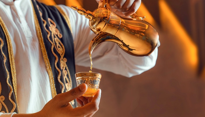 Traditional Arabic coffee being poured from a golden pot into an ornate cup.