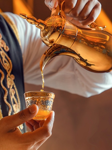 Traditional Arabic coffee being poured from a golden pot into an ornate cup.