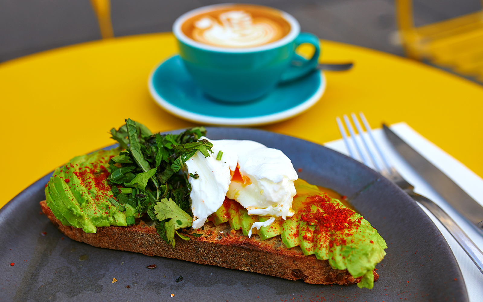 Flat white coffee and avocado toast on a table with Hop On Hop Off Belfast bus in the background.