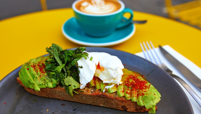 Flat white coffee and avocado toast on a table with Hop On Hop Off Belfast bus in the background.
