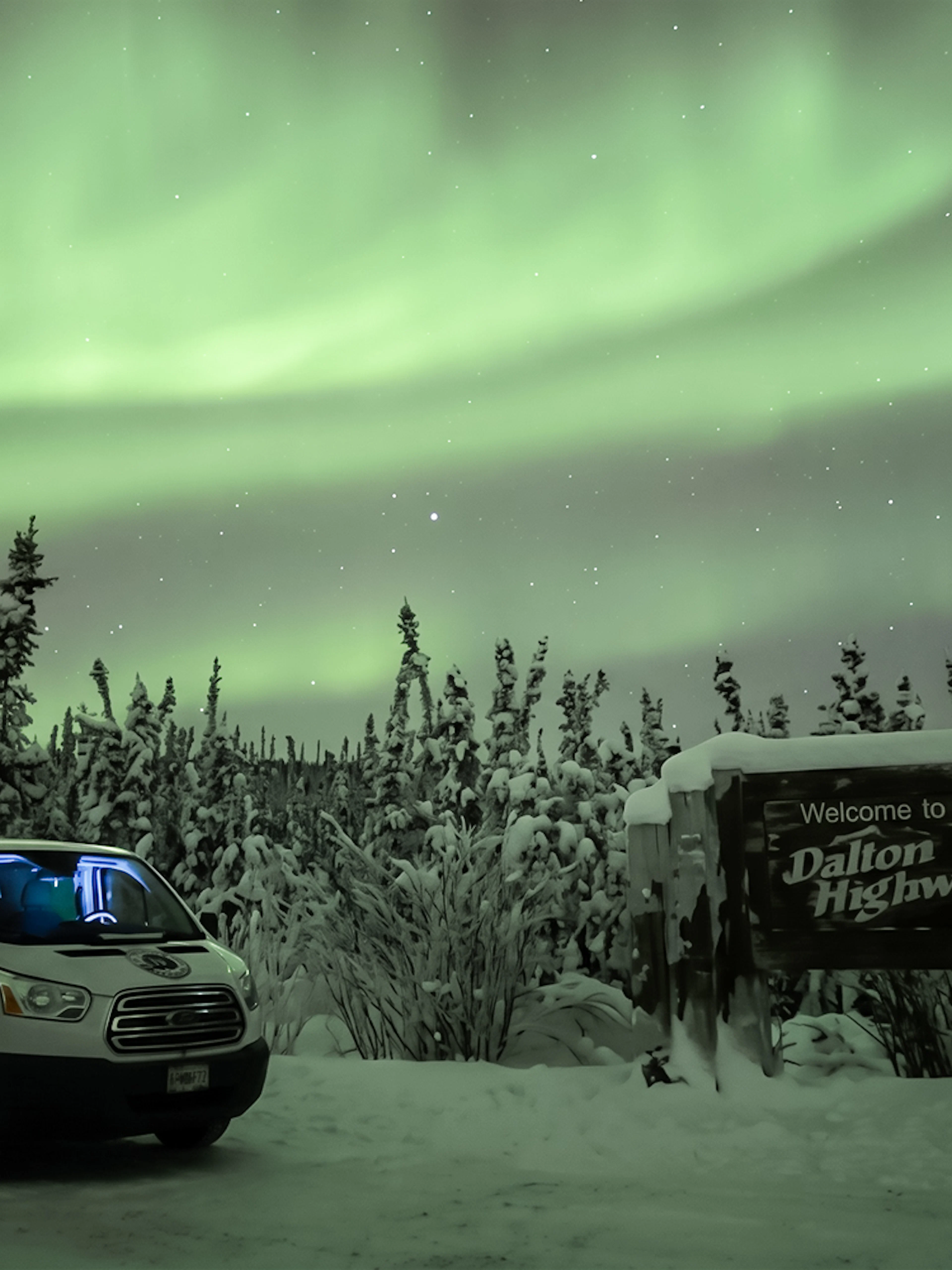 Van parked under Northern Lights near Dalton Highway sign, Alaska.