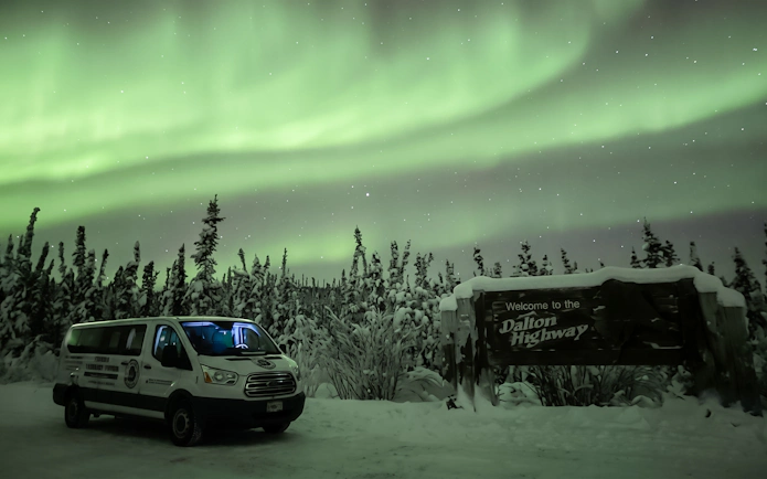 Van parked under Northern Lights near Dalton Highway sign, Alaska.