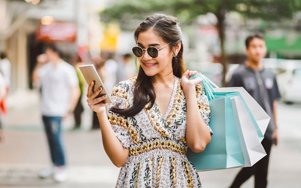 Woman using smartphone with shopping bags in Thailand street.