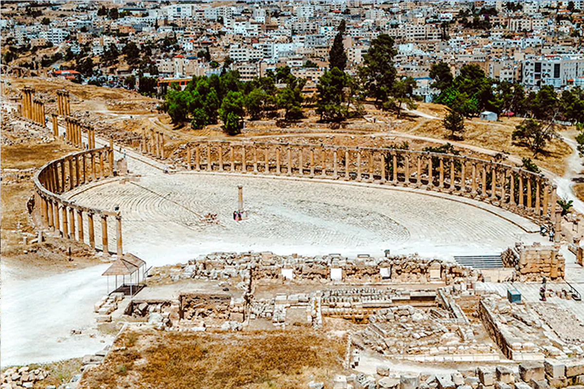 Roman oval plaza in Jerash with ancient columns and cityscape in the background.