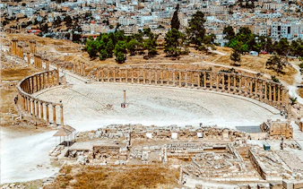Roman oval plaza in Jerash with ancient columns and cityscape in the background.