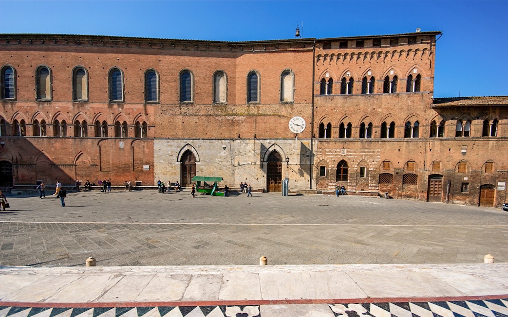 Santa Maria della Scala museum facade in Siena, Italy, with visitors in the courtyard.