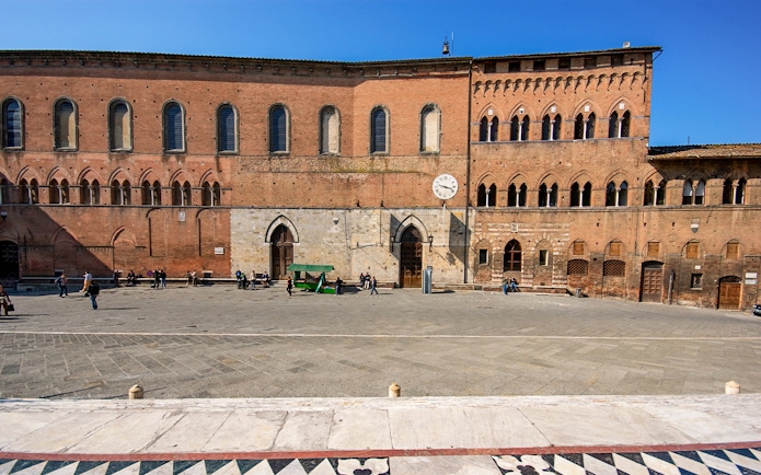 Santa Maria della Scala museum facade in Siena, Italy, with visitors in the courtyard.
