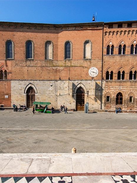 Santa Maria della Scala museum facade in Siena, Italy, with visitors in the courtyard.