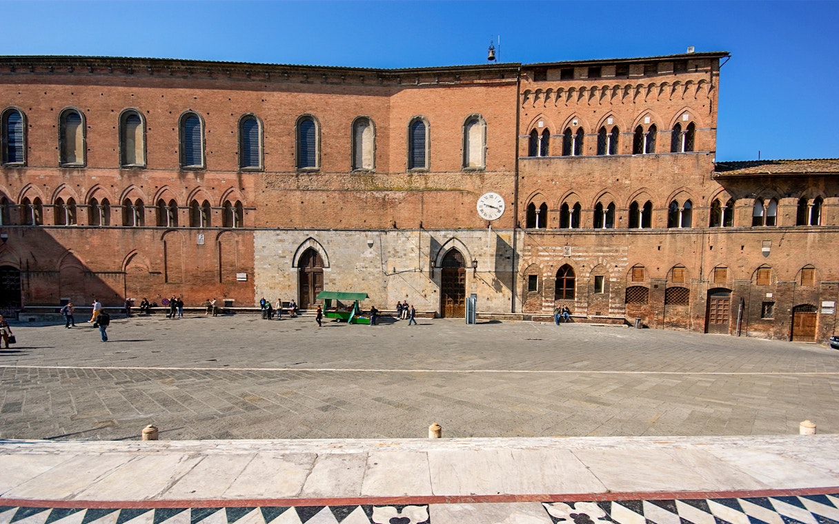 Santa Maria della Scala museum facade in Siena, Italy, with visitors in the courtyard.