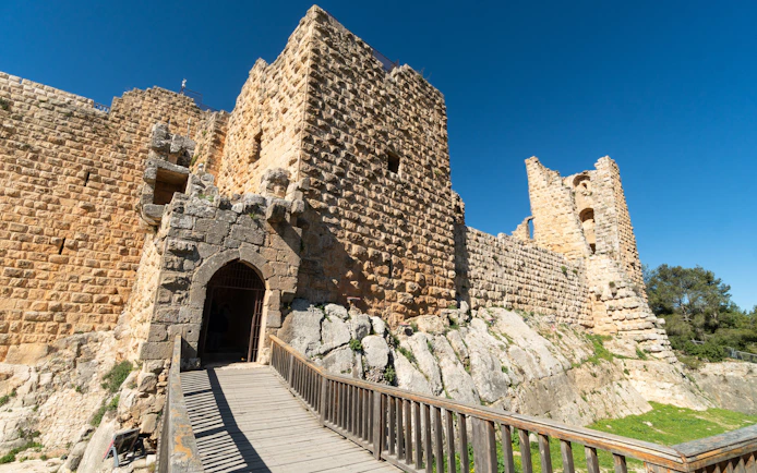 Ajloun Castle stone walls and entrance bridge under clear blue sky in Jordan.