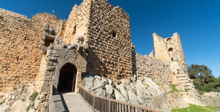 Ajloun Castle stone walls and entrance bridge under clear blue sky in Jordan.