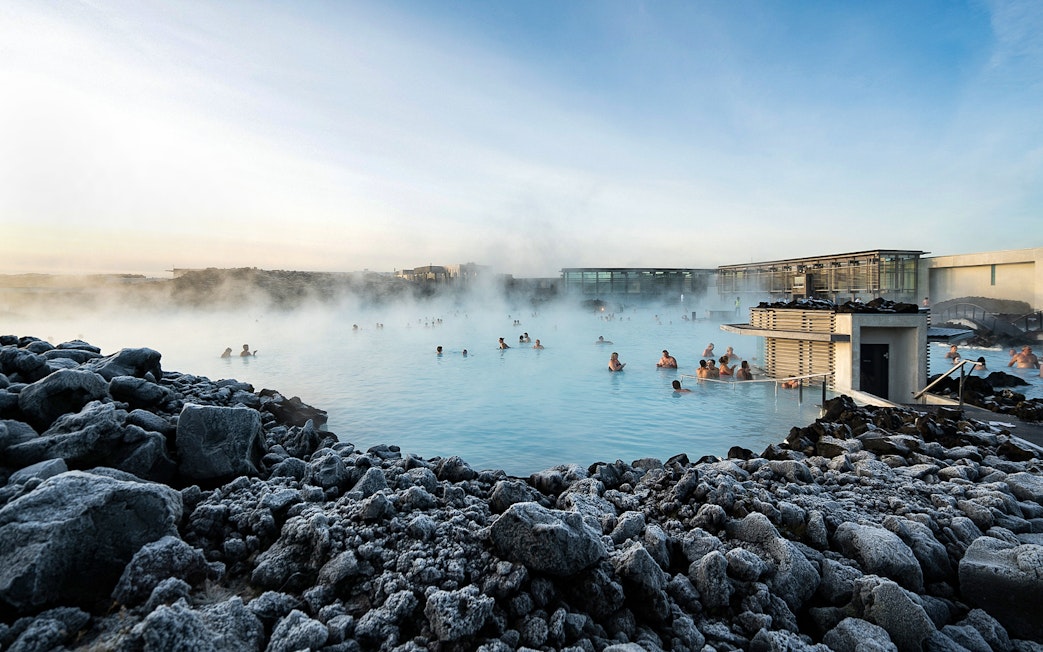 People enjoying the Blue Lagoon geothermal pool surrounded by rocky landscape in Iceland.