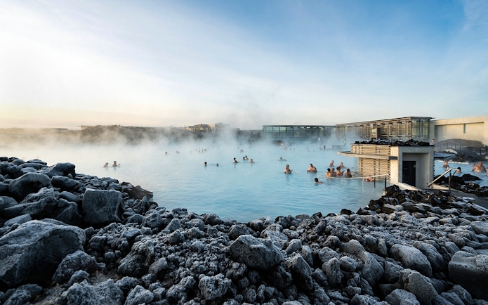 People enjoying the Blue Lagoon geothermal pool surrounded by rocky landscape in Iceland.