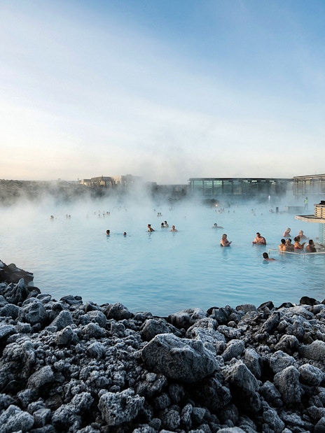 People enjoying the Blue Lagoon geothermal pool surrounded by rocky landscape in Iceland.