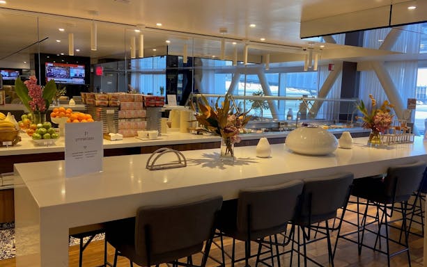 Primeclass Lounge dining area with snacks and fruit at JFK Airport, New York.