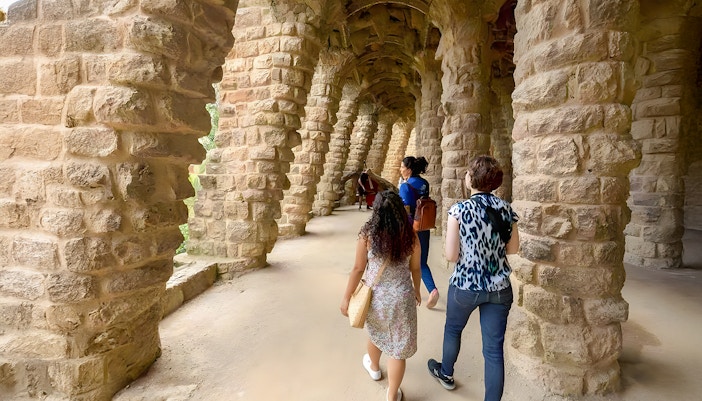Tourist with guide exploring Park Güell's colorful mosaic structures in Barcelona.