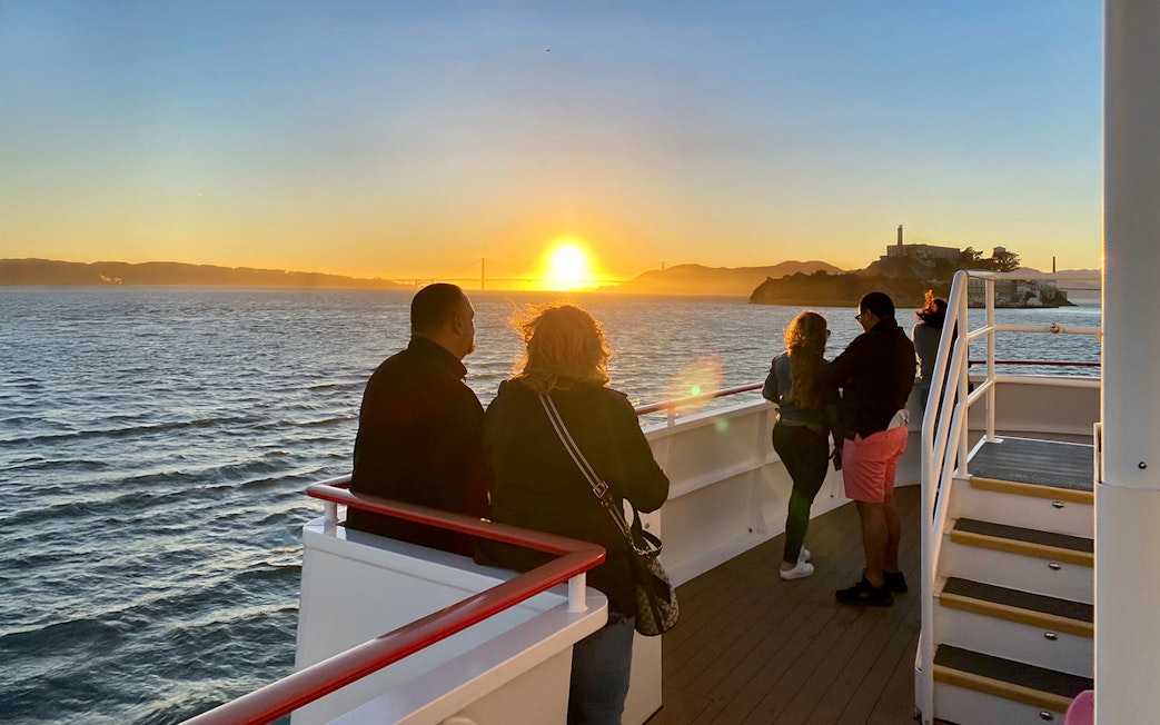 Guests on deck watching sunset during California cruise with Golden Gate Bridge in view.