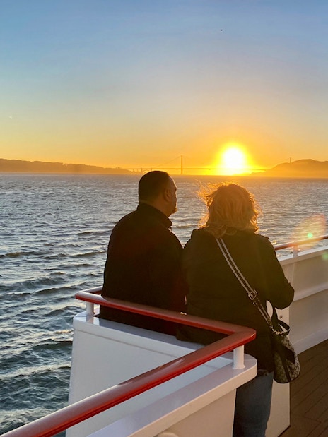 Guests on deck watching sunset during California cruise with Golden Gate Bridge in view.