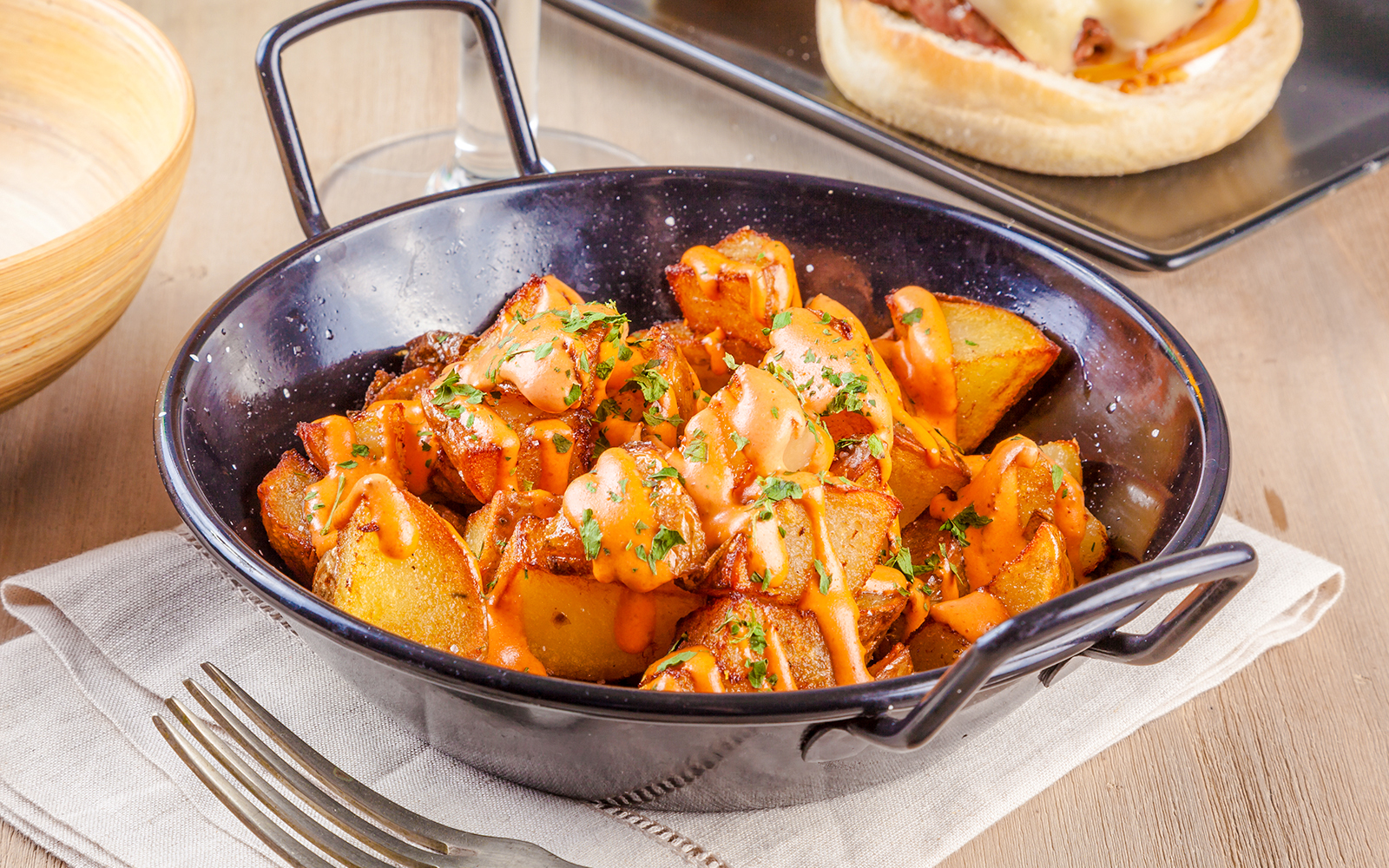 Patatas bravas with spicy sauce and herbs in a black dish.