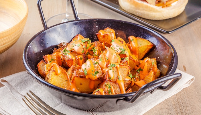 Patatas bravas with spicy sauce and herbs in a black dish.