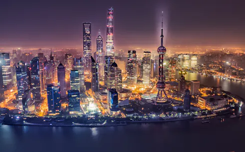 Shanghai skyline at night featuring the Oriental Pearl Tower and illuminated skyscrapers.
