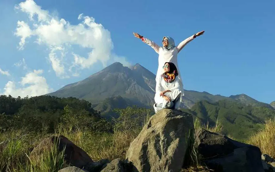 Two people on rocks with Mount Merapi in the background during sunrise, Jeep Merapi Lava Tour.
