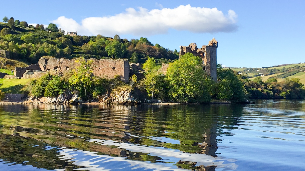 Urquhart Castle viewed from the lake with surrounding greenery.