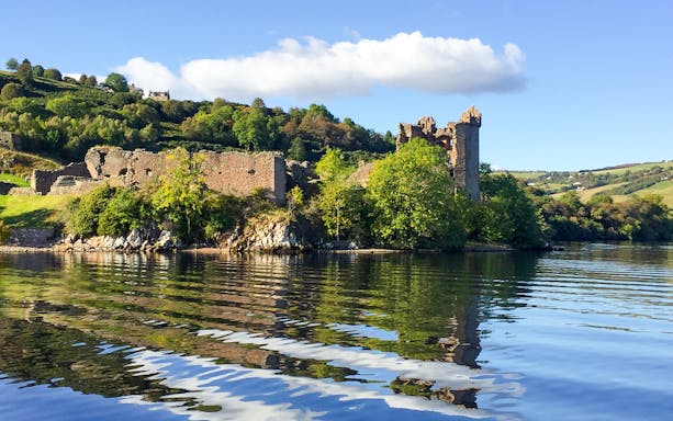 Urquhart Castle viewed from the lake with surrounding greenery.