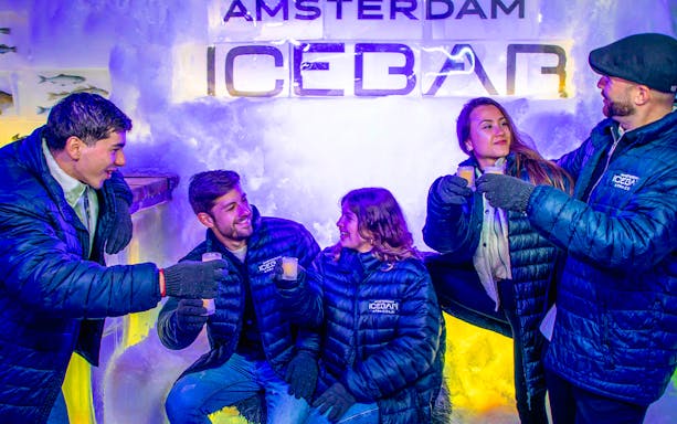 Visitors enjoying drinks at Icebar Amsterdam in winter coats.