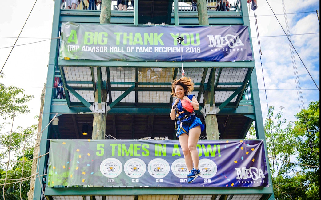 Person ziplining at Mega Adventure Park, Singapore, with banners in the background.