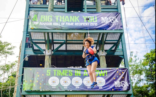 Person ziplining at Mega Adventure Park, Singapore, with banners in the background.