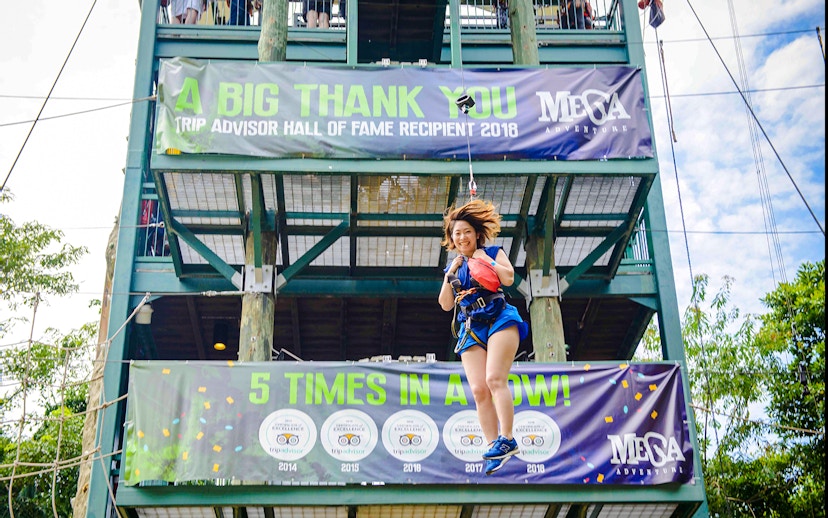 Person ziplining at Mega Adventure Park, Singapore, with banners in the background.