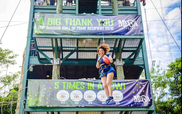 Person ziplining at Mega Adventure Park, Singapore, with banners in the background.