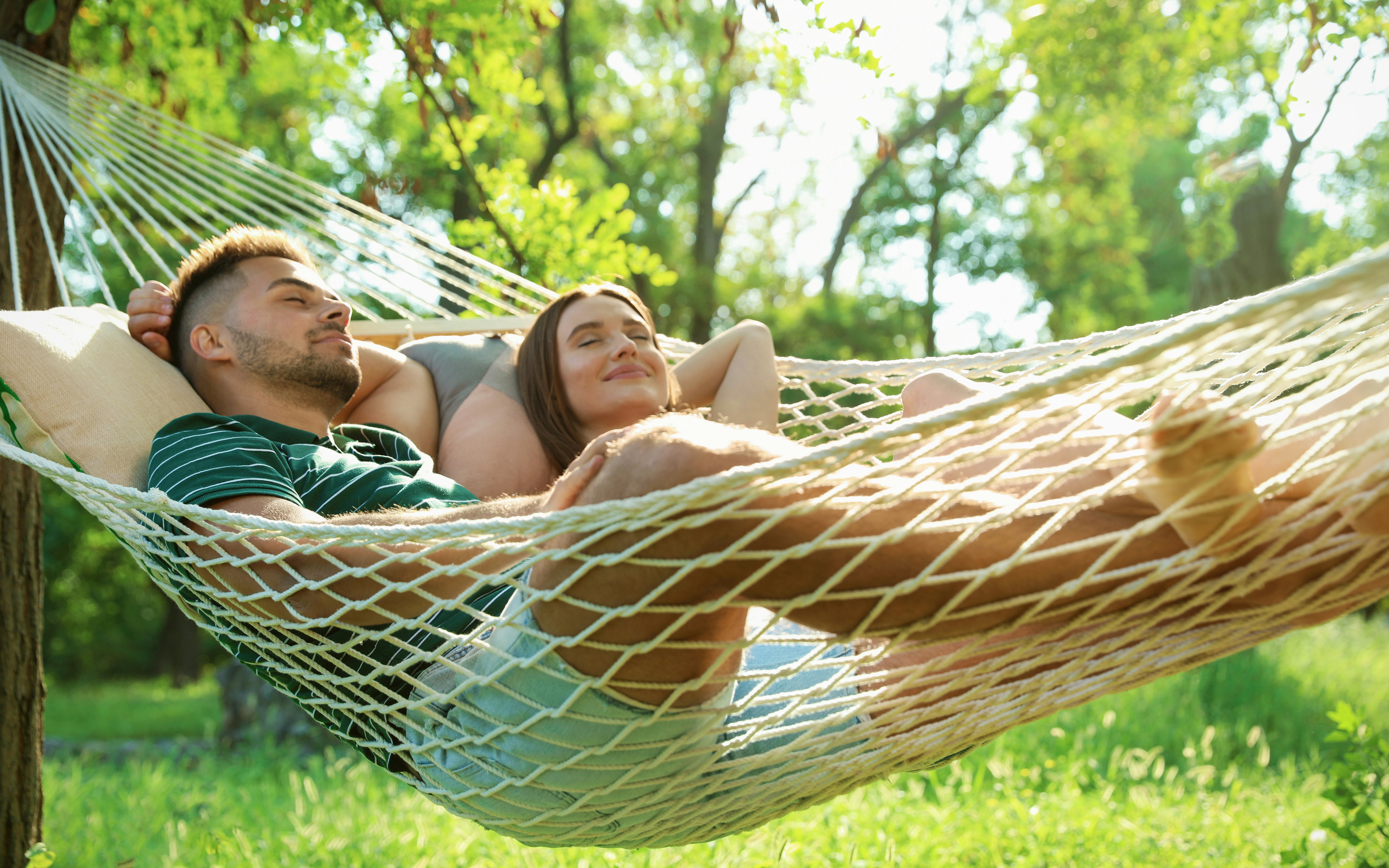 Young couple relaxing in a hammock in a sunny, green park.