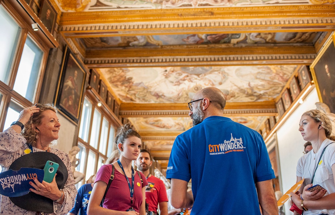 Engaged tour group with guide inside the Uffizi Gallery, surrounded by Renaissance masterpieces and intricate ceiling frescoes in Florence