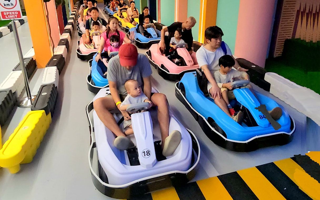Families driving colorful go-karts through a rainbow archway at VroomTown Driving City.