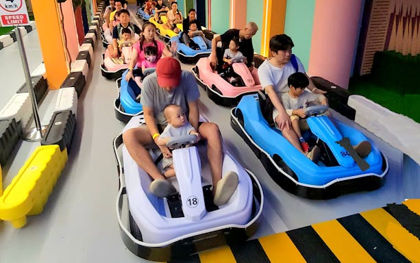 Families driving colorful go-karts through a rainbow archway at VroomTown Driving City.