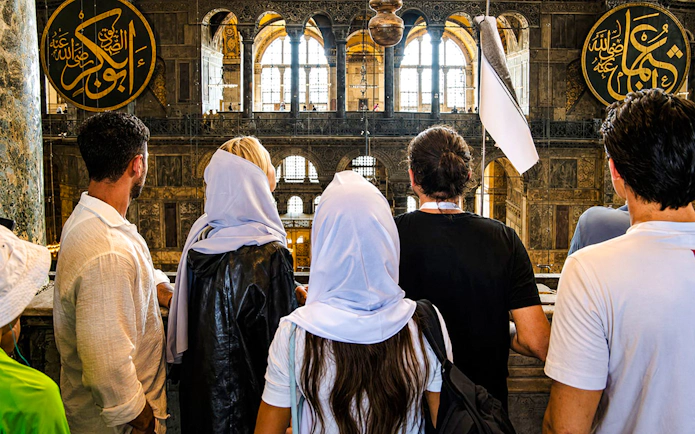 Visitors inside Hagia Sophia, Istanbul, viewing ornate interior and calligraphy.