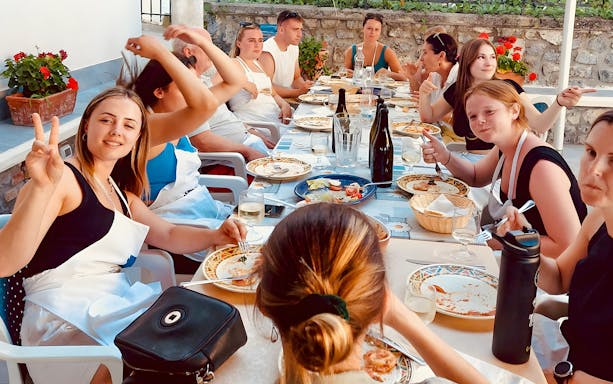 Group enjoying Italian cooking class meal on Amalfi Coast terrace.