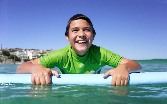 Child enjoying surf lesson at Bondi Beach, holding a surfboard in the water.